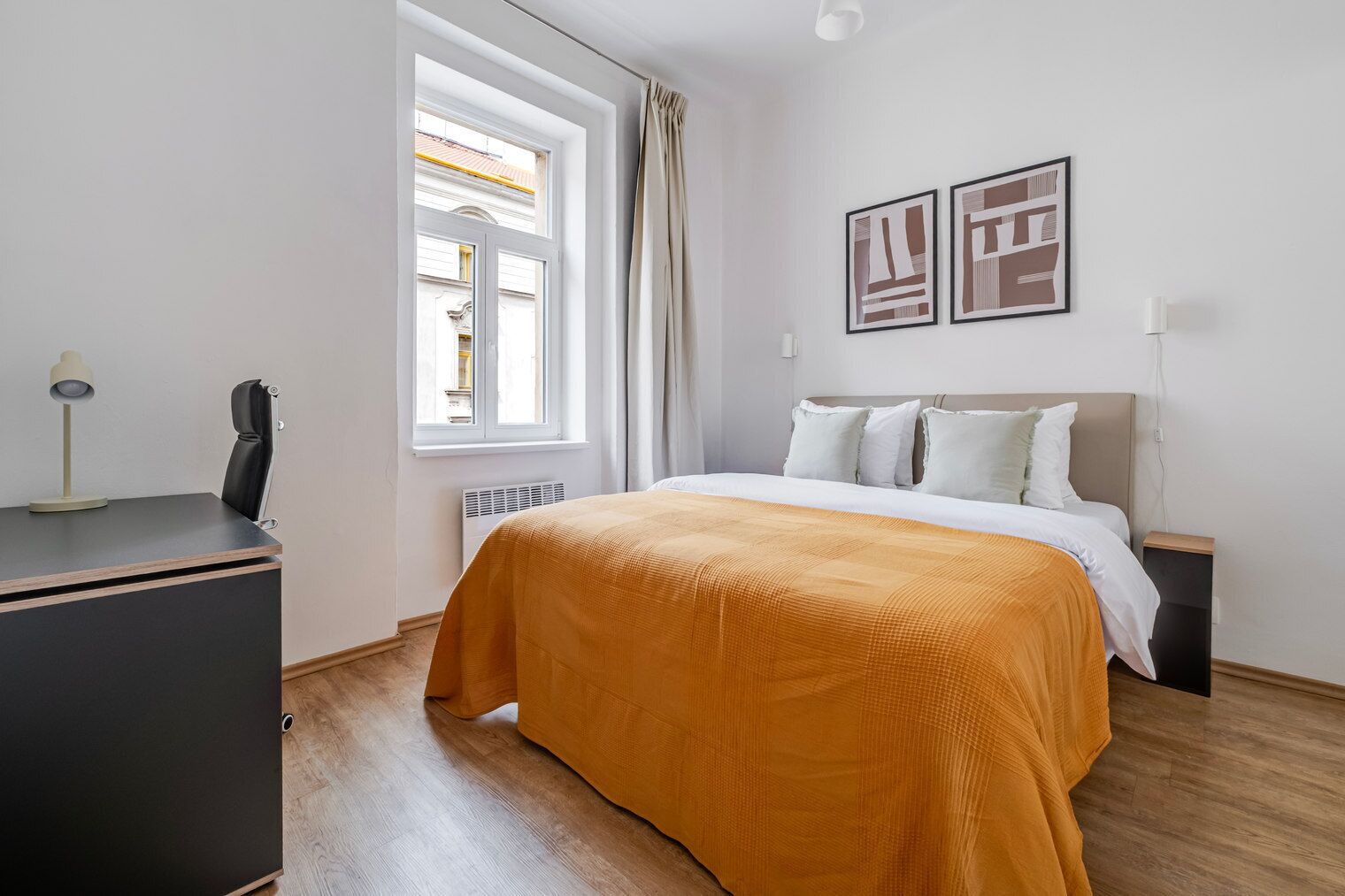 Un dormitorio con cama, escritorio, silla, radiador y ventana con cortinas.