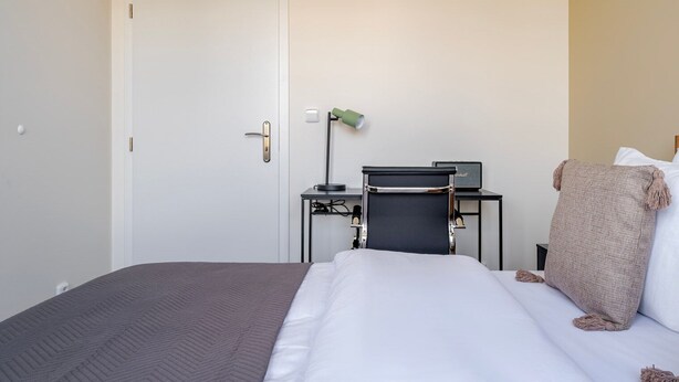 A hotel room with a bed, a desk, a chair, a lamp, and a blanket. - Blueground | Nusle, city view, nr Vysehrad (PRG-108) (Prague)