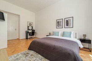 A bedroom with a bed, a desk, and a chair. There are two framed pictures on the wall. - Blueground | Vinohrady, view, nr Riegrovy Sady (PRG-110) (Prague)