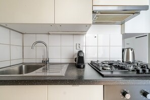A modern kitchen with a stainless steel sink, a built-in range hood, and a gas stove. - Blueground | Vinohrady, view, nr Riegrovy Sady (PRG-110) (Prague)