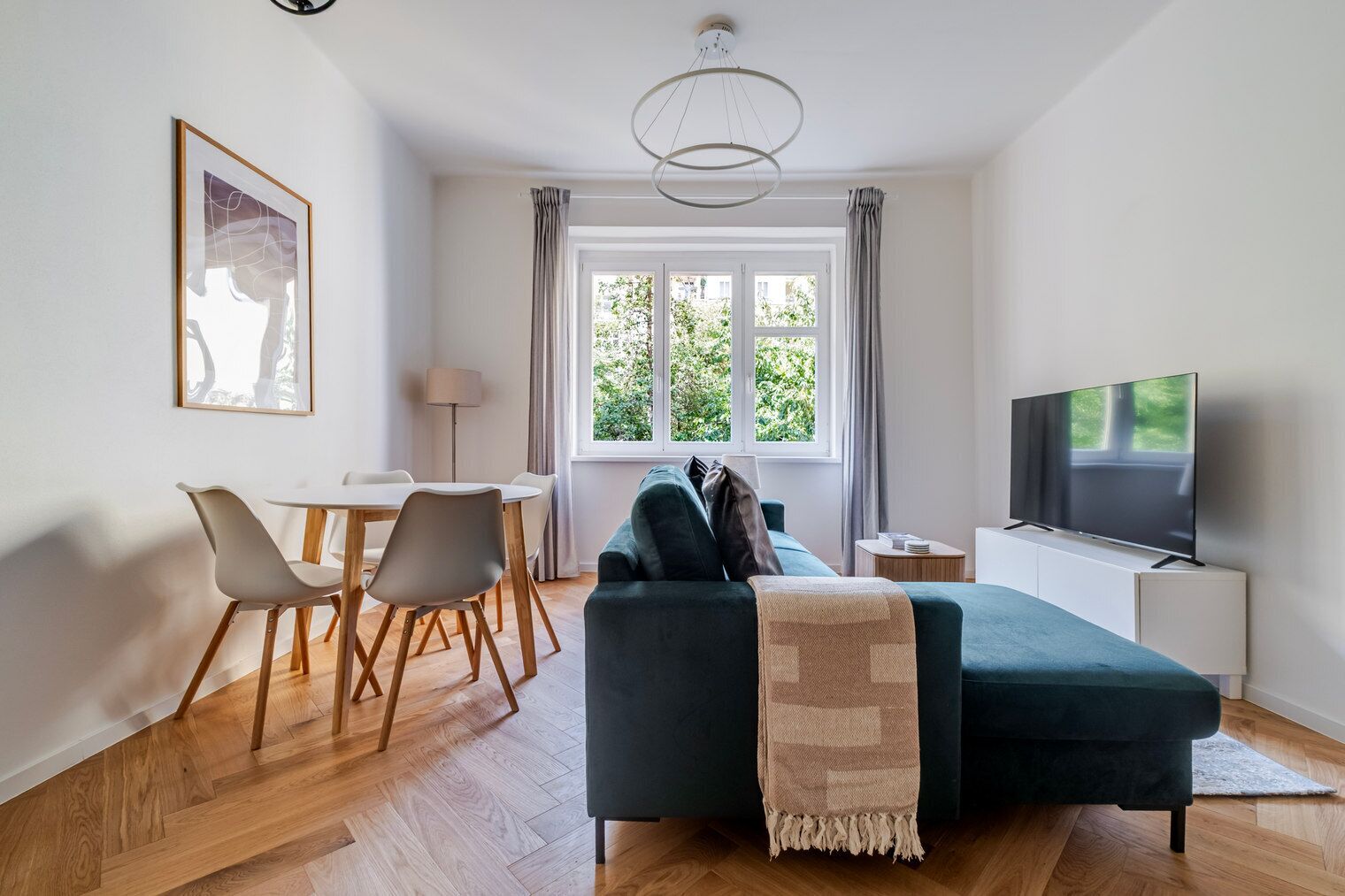 Un salon moderne avec un canapé, un téléviseur, un coin repas et de grandes fenêtres.