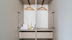 Vaatehuoneessa on kaksi puista henkaria, pino valkoisia, taiteltuja pyyhkeitä sekä keltainen ja valkoinen silityslauta.
