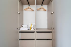 A walk-in closet with two wooden hangers, a stack of folded white towels, and a yellow and white iron. - Blueground | Vinohrady, view, nr Vysehrad (PRG-109) (Prague)