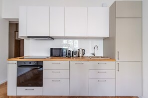 A modern kitchen with white cabinets, a wooden countertop, a built-in oven, a microwave, a kettle, and a sink. - Blueground | Vinohrady, view, nr Vysehrad (PRG-109) (Prague)