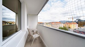 A balcony with a white chair and table, a window, and a view of buildings and construction. - Blueground | Pankrác, view, spacious, near offices (PRG-113) (Prague)