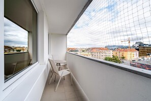 Ein Balkon mit weißem Stuhl und Tisch, einem Fenster und Blick auf Gebäude und eine Baustelle.