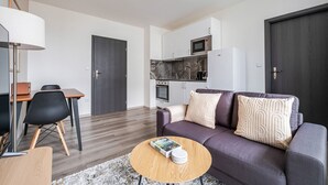 A modern living room with a sofa, coffee table, and a dining area with chairs. - Blueground | Pankrác, view, spacious, near offices (PRG-113) (Prague)