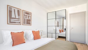 Ein modernes Schlafzimmer mit einem großen Bett, einem Kleiderschrank und zwei gerahmten Kunstwerken an der Wand.