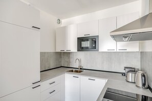 A modern kitchen with white cabinetry, a stainless steel sink, a built-in microwave, and a kettle. - Blueground | Žižkov, garden view, nr Vitkov (PRG-114) (Prague)