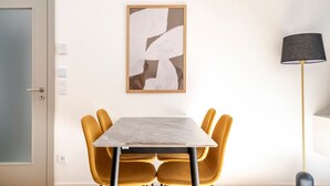 Een eethoek met een tafel en stoelen, een aan de muur hangend abstract schilderij, een vloerlamp en een deur met een deurklink.