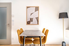 Ein Essbereich mit Tisch und Stühlen, einem an der Wand hängenden abstrakten Gemälde, einer Stehlampe und einer Tür mit Griff.