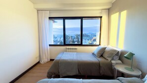 A bedroom with a large window, a bed, a bedside table with a lamp, and a radiator. - El Coral - Lake View Apartment · Great Location in San Carlos de Bariloche (San Carlos de Bariloche)