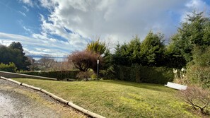 A grassy area with a bench, a wooden fence, and a variety of trees. - El Coral - Lake View Apartment · Great Location in San Carlos de Bariloche (San Carlos de Bariloche)