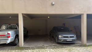 Un garaje de estacionamiento con dos vehículos, una camioneta pickup y un sedán, estacionados bajo un edificio con piso de concreto y una puerta marcada con el número 03.