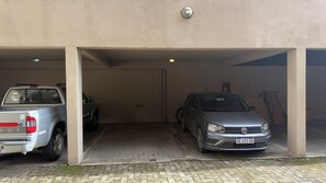 A parking garage with two vehicles, a pickup truck and a sedan, parked under a building with a concrete floor and a door marked with the number 03. - El Coral - Lake View Apartment · Great Location in San Carlos de Bariloche (San Carlos de Bariloche)