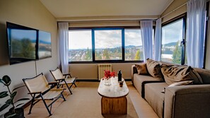 A living room with a sofa, chairs, a coffee table, and a view of a cityscape through large windows. - El Coral - Lake View Apartment · Great Location in San Carlos de Bariloche (San Carlos de Bariloche)