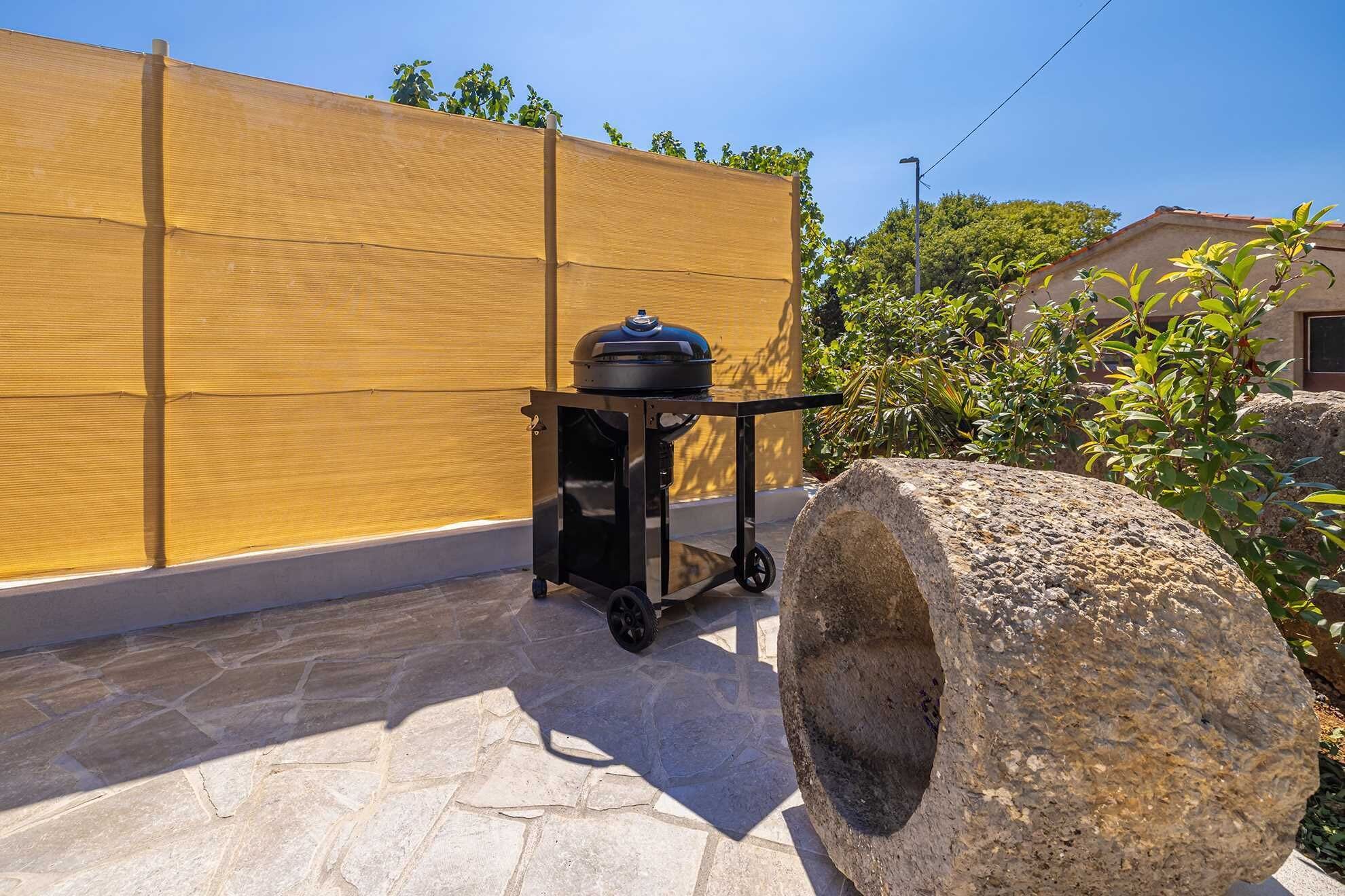 A patio with a stone floor, a barbecue grill on a wheeled cart, and a large stone feature.