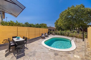 A swimming pool with a stone deck, a table with chairs, and a wooden fence. - Holiday house SAN LEONARDO with private pool (Bajčići)