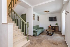 A staircase with green balusters leading to a landing, a green sofa, a small round table with a vase, and a flat-screen TV mounted on the wall. - Holiday house SAN LEONARDO with private pool (Bajčići)