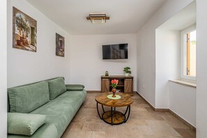 A living room with a green sofa, a round wooden table with a vase, and a TV mounted on the wall. - Holiday house SAN LEONARDO with private pool (Bajčići)