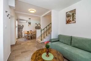 A living room with a green sofa, a wooden coffee table with a vase of flowers, and a staircase leading to a dining area. - Holiday house SAN LEONARDO with private pool (Bajčići)