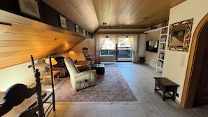 A spacious living area with a high ceiling, a fireplace, a large window, and a bookshelf. - Silvia Vacation Rental (Bischofswiesen)