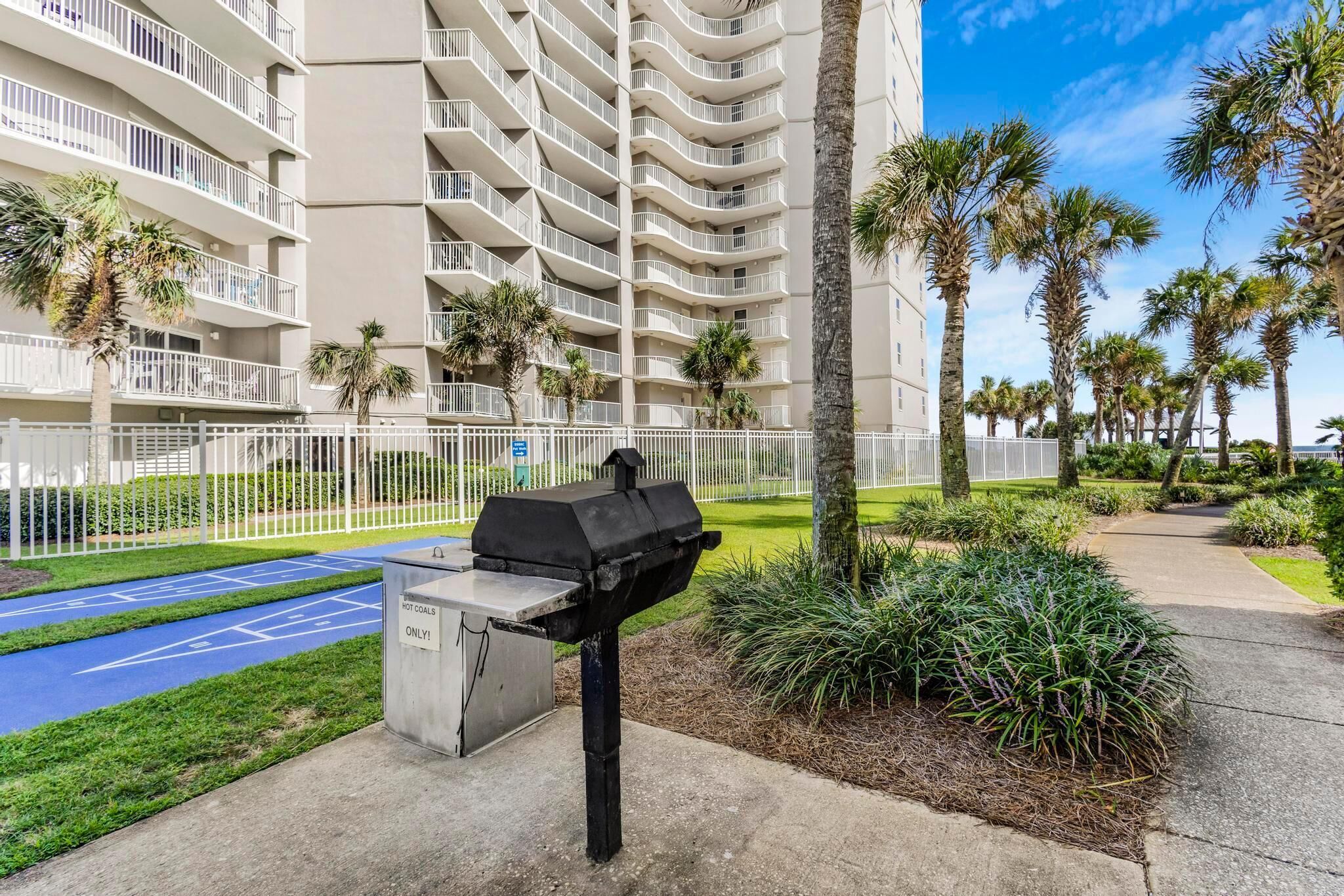 A residential building with multiple balconies, a barbecue grill, and a tennis court.