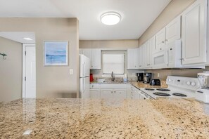 A kitchen with white cabinets, a granite countertop, a refrigerator, a stove, and a coffee maker. - Seaside Beach & Racquet 5517 (Orange Beach)
