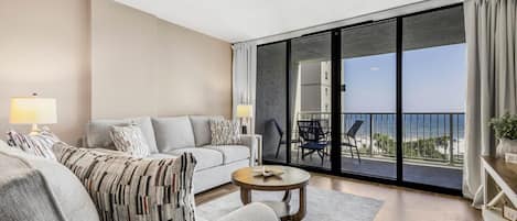 A modern living room with a sofa, coffee table, and a view of the ocean through large glass doors.
