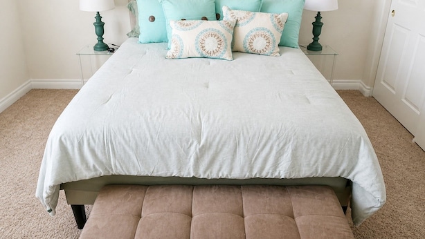 A bed with a light-colored duvet, multiple pillows, and a bench at the foot of the bed.
