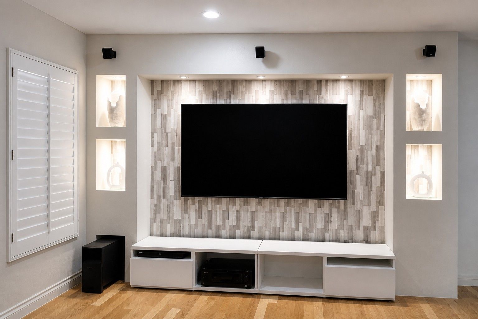 A modern living room with a large flat-screen TV mounted on a wooden wall, a white entertainment unit below, and recessed lighting.