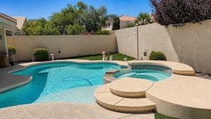 A swimming pool with a curved design, surrounded by a low wall and a grassy area.