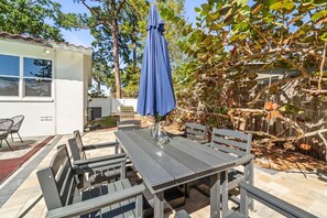 An outdoor patio with a table and chairs, a blue umbrella, and a wooden fence. - Game Room, Pool & Fire Pit Near Madeira Beach (Seminole)