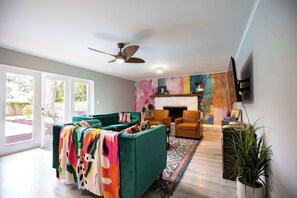 A living room with a green sofa set, a fireplace, and a colorful abstract wall art. - Game Room, Pool & Fire Pit Near Madeira Beach (Seminole)