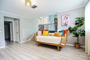 Uma sala de estar com um sofá de vime, uma planta grande e um quadro na parede.