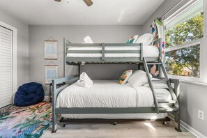 Een stapelbed met een ladder, een kruipzak en twee kunstwerken in lijsten aan de muur.