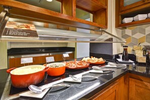 Ein reichhaltiges Buffet mit beschrifteten Speisen, einer Edelstahl-Dunstabzugshaube und Holzschränken.