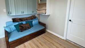 Ein Zimmer mit Holzboden, einem blauen Sofa mit Kissen, hellblauen Schränken und einer weißen Tür.