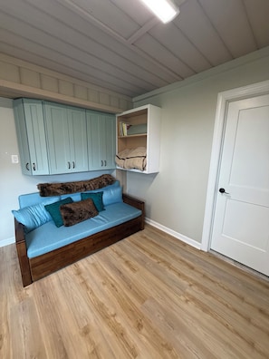 A room with a wooden floor, a blue sofa with cushions, light blue cabinets, and a white door. - MarshMellow -Peaceful Knott's Island Waterfront Retreat (knotts island)