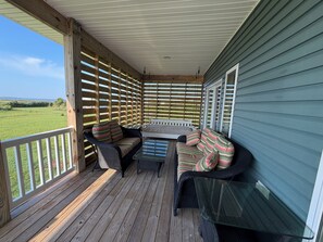 A covered porch with a wooden floor, two wicker sofas with striped cushions, and a glass table. - MarshMellow -Peaceful Knott's Island Waterfront Retreat (knotts island)