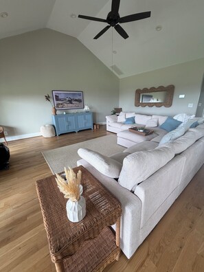 A spacious living room with a high ceiling, a ceiling fan, a light-colored sofa set, a blue cabinet, and a framed picture on the wall. - MarshMellow -Peaceful Knott's Island Waterfront Retreat (knotts island)