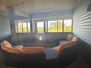 A covered outdoor seating area with two wicker chairs and a view of a green landscape. - MarshMellow -Peaceful Knott's Island Waterfront Retreat (knotts island)