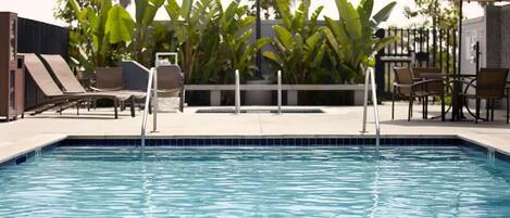 A swimming pool with lounge chairs and a table, surrounded by greenery.