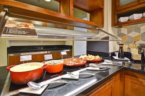 Ein reichhaltiges Buffet mit beschrifteten Speisen, einer Edelstahl-Dunstabzugshaube und Holzschränken.
