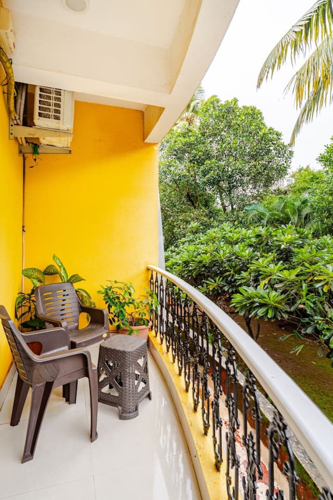 A balcony with a yellow wall, a white railing, and potted plants.