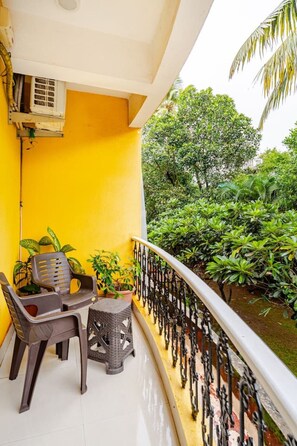 A balcony with a yellow wall, a white railing, and potted plants.