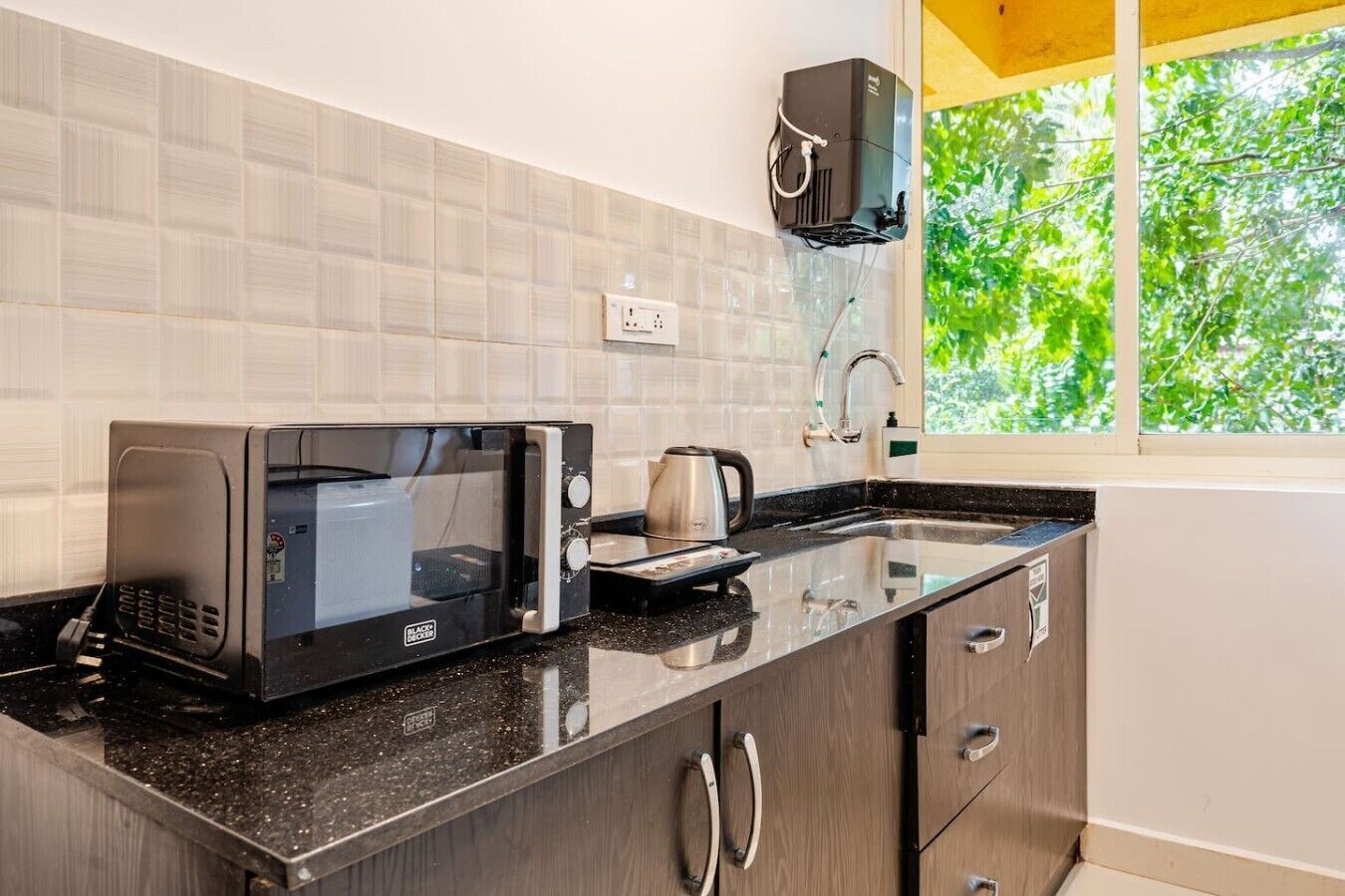 Uma cozinha com micro-ondas, chaleira e janela com vista para o verde.