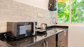 Uma cozinha com micro-ondas, chaleira e janela com vista para o verde.