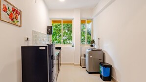 A compact kitchen with a refrigerator, a washing machine, and a trash bin.