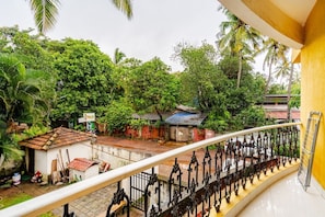 Un balcon donnant sur une petite maison, un jardin et un palmier.